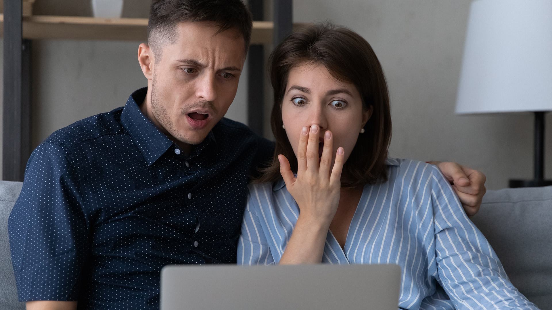 junges Paar vor Laptop mit erschrockenem Gesichtsausdruck